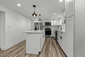 Kitchen with white cabinetry, stainless steel appliances, light wood-style flooring, and a kitchen island