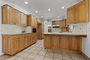 Kitchen with light countertops, a peninsula, light tile patterned floors, wood finish cabinetry, and recessed lighting