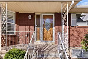 View of exterior entry with covered porch and brick siding