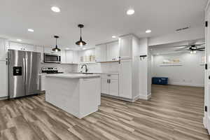 Kitchen with stainless steel appliances, white cabinetry, light wood-style flooring, and a center island