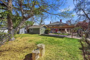 Back of property with an outbuilding, a chimney, a patio, and roof with shingles