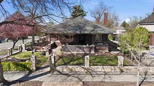 Rear view of house featuring a shingled roof, a fenced front yard, brick siding, a chimney, and a patio area