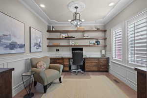 Home office with a decorative wall, light wood-style floors, wainscoting, built in study area, and hanging lights