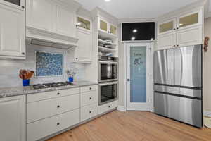 Kitchen featuring stainless steel appliances, white cabinetry, glass fronted cabinets, light stone countertops, and light wood-style flooring