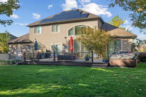Back of house featuring a deck, solar panels, a hot tub, a yard, and stucco siding