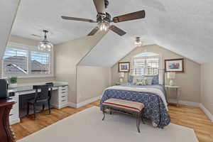 Bedroom with a textured ceiling, light wood-style flooring, multiple windows, ceiling fan, and a desk