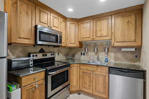Kitchen featuring stainless steel appliances, dark stone countertops, wood finish cabinets, and backsplash