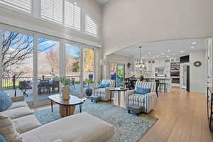Living room featuring crown molding, light wood-type flooring, arched walkways, a high ceiling, and a chandelier