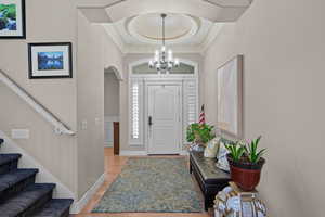 Foyer entrance with a raised ceiling, light wood-type flooring, arched walkways, hanging lights, and ornamental molding