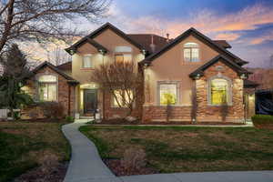 View of front of home with stone siding, a yard, and stucco siding