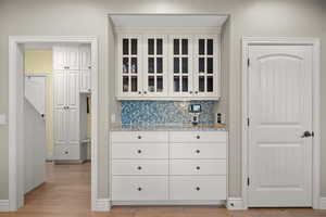 Kitchen with light stone counters, glass fronted cabinets, backsplash, and light wood-style floors