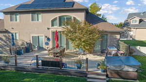 Rear view of house with roof mounted solar panels, stucco siding, a wooden deck, a patio, and roof with shingles