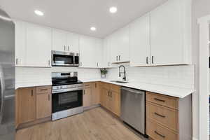 Kitchen featuring stainless steel appliances, dual tone cabinets, light wood-style floors, light stone counters, and decorative backsplash