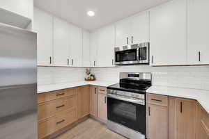 Kitchen featuring stainless steel appliances, backsplash, recessed lighting, light wood-type flooring, and two tone color scheme
