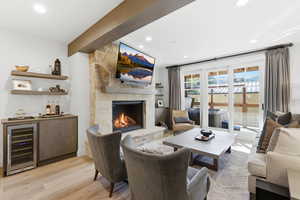 Living area featuring wine cooler, a stone fireplace, light wood-style flooring, recessed lighting, and a dry bar