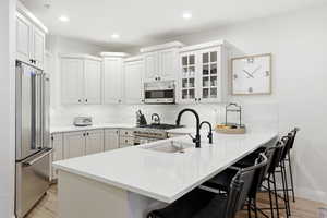Kitchen featuring a breakfast bar, a peninsula, high quality appliances, white cabinets, and recessed lighting