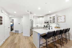Kitchen with a breakfast bar, glass insert cabinets, a peninsula, white cabinetry, and light wood finished floors