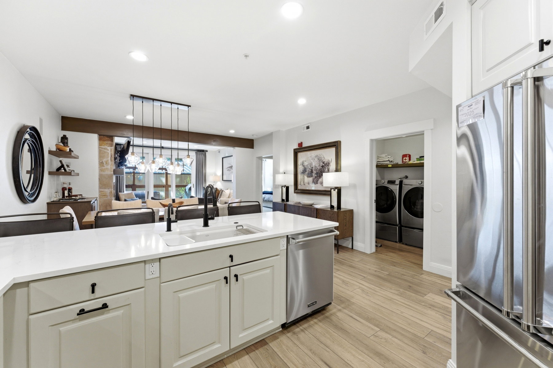 Kitchen with stainless steel appliances, washing machine and dryer, light wood-style floors, white cabinets, and light stone countertops