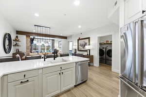 Kitchen with stainless steel appliances, washing machine and dryer, light wood-style floors, white cabinets, and light stone countertops