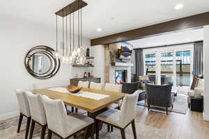 Dining space featuring beam ceiling, light wood-style floors, a stone fireplace, and recessed lighting