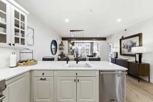 Kitchen featuring dishwasher, glass insert cabinets, light stone counters, pendant lighting, and light wood-style floors