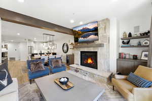 Living area featuring light wood-type flooring, a stone fireplace, beamed ceiling, recessed lighting, and beverage cooler