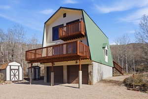 Back of house featuring a storage shed, an attached garage, gravel driveway, and a wooden deck