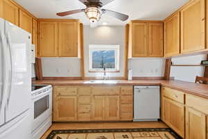 Kitchen with white appliances, light countertops, ceiling fan, and light wood finish cabinetry