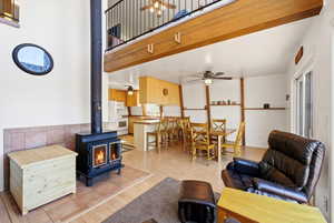 Living room with a wood stove, a ceiling fan, a high ceiling, and light wood-type flooring