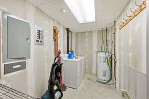 Laundry room featuring a paneled ceiling, concrete flooring, electric panel, water heater, and independent washer and dryer