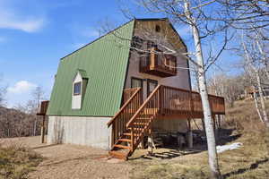 Back of property with a gambrel roof, a deck, a metal roof, and a balcony