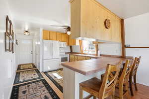 Kitchen with a kitchen bar, white appliances, a peninsula, a ceiling fan, and light wood finish cabinetry