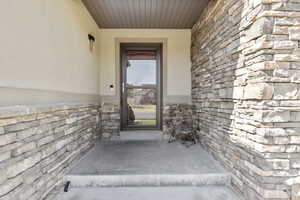 View of exterior entry featuring stone siding and a patio
