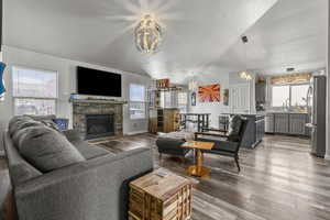Living area with vaulted ceiling, dark wood-type flooring, a stone fireplace, and hanging lights