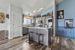 Kitchen featuring gray cabinetry, stainless steel appliances, a center island, lofted ceiling, and a kitchen bar