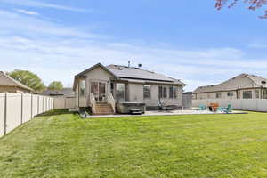 Rear view of property with roof mounted solar panels, entry steps, a patio area, a fenced backyard, and a hot tub