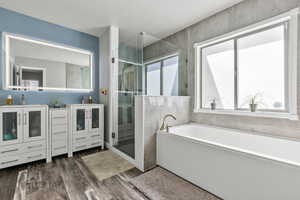 Full bathroom featuring a shower stall, a bath, double vanity, and dark wood-style flooring