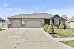 View of front of house featuring stucco siding, an attached garage, concrete driveway, stone siding, and a front lawn