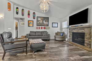 Living room featuring wood finished floors, lofted ceiling, and a stone fireplace