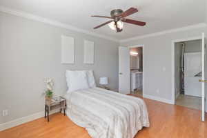 Bedroom with light wood-style flooring, ornamental molding, a ceiling fan, and connected bathroom