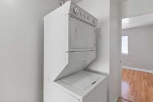 Laundry area with light wood-type flooring and stacked washing machine and dryer