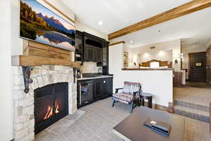Living room featuring a stone fireplace, recessed lighting, and beam ceiling