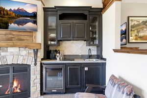 Kitchen featuring glass fronted cabinets, light stone countertops, tasteful backsplash, beverage cooler, and dark cabinetry
