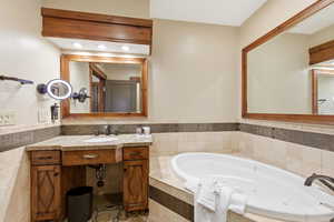 Bathroom featuring vanity, a jetted tub, and tile walls
