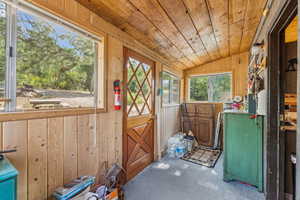 Doorway to outside featuring a vaulted wood ceiling, wooden walls, and carpet floors