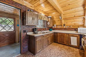 Kitchen with light countertops, a wooden ceiling with exposed beams, light colored carpet, white microwave, and wooden walls