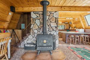 Detailed view of a wood ceiling with exposed beams, carpet floors, wooden walls, a wood stove, and a smoke detector