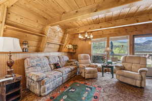 Living room featuring hanging lights, wooden walls, carpet, and a wooden ceiling with exposed beams