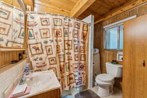 Bathroom with vanity, wooden walls, shower / tub combo, and wood ceiling