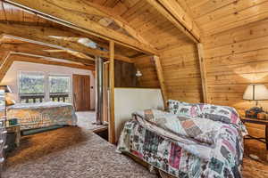 Carpeted bedroom with a wood ceiling with exposed beams and wood walls